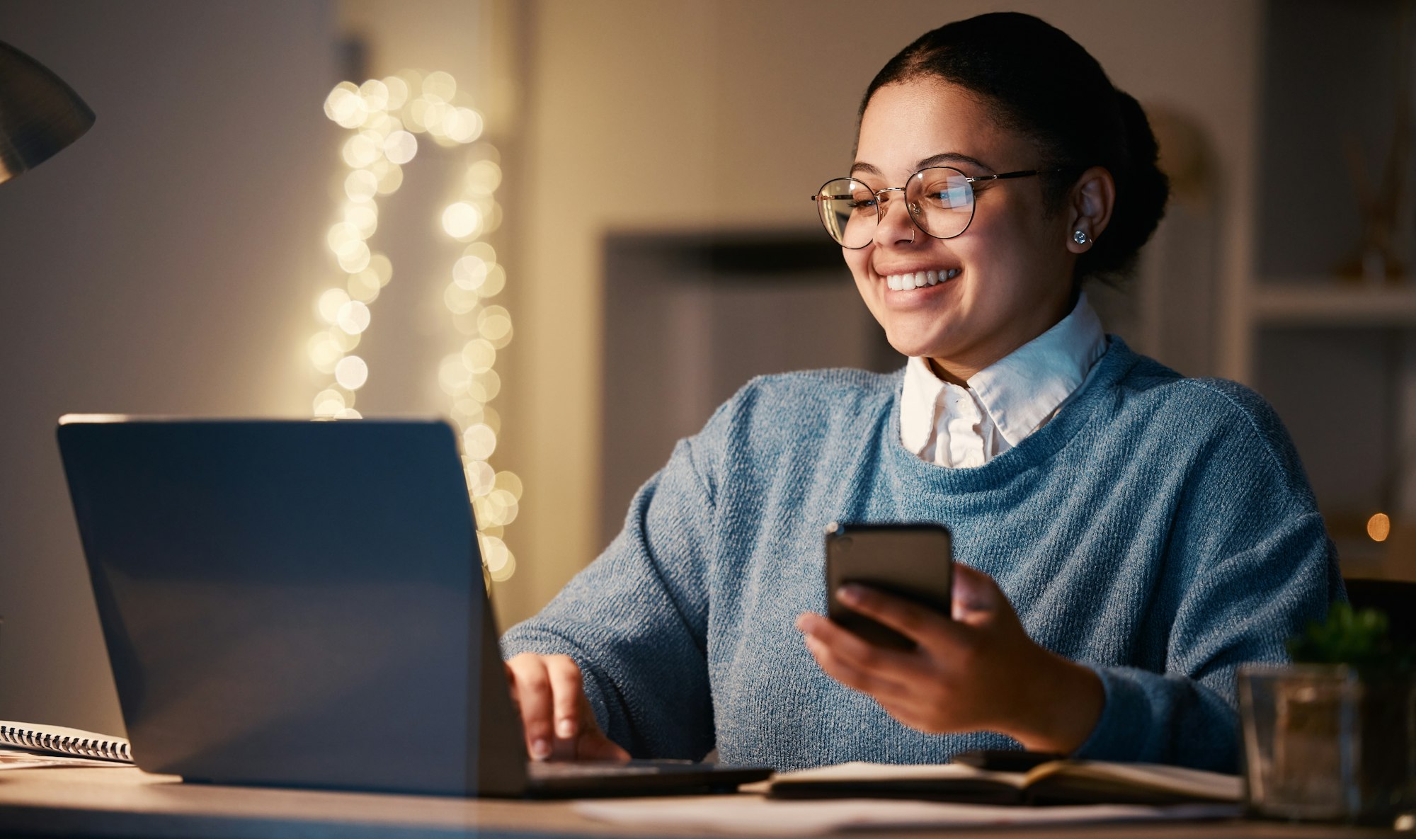 Woman, phone and student with laptop in home for web browsing, project or studying at night. Bokeh,